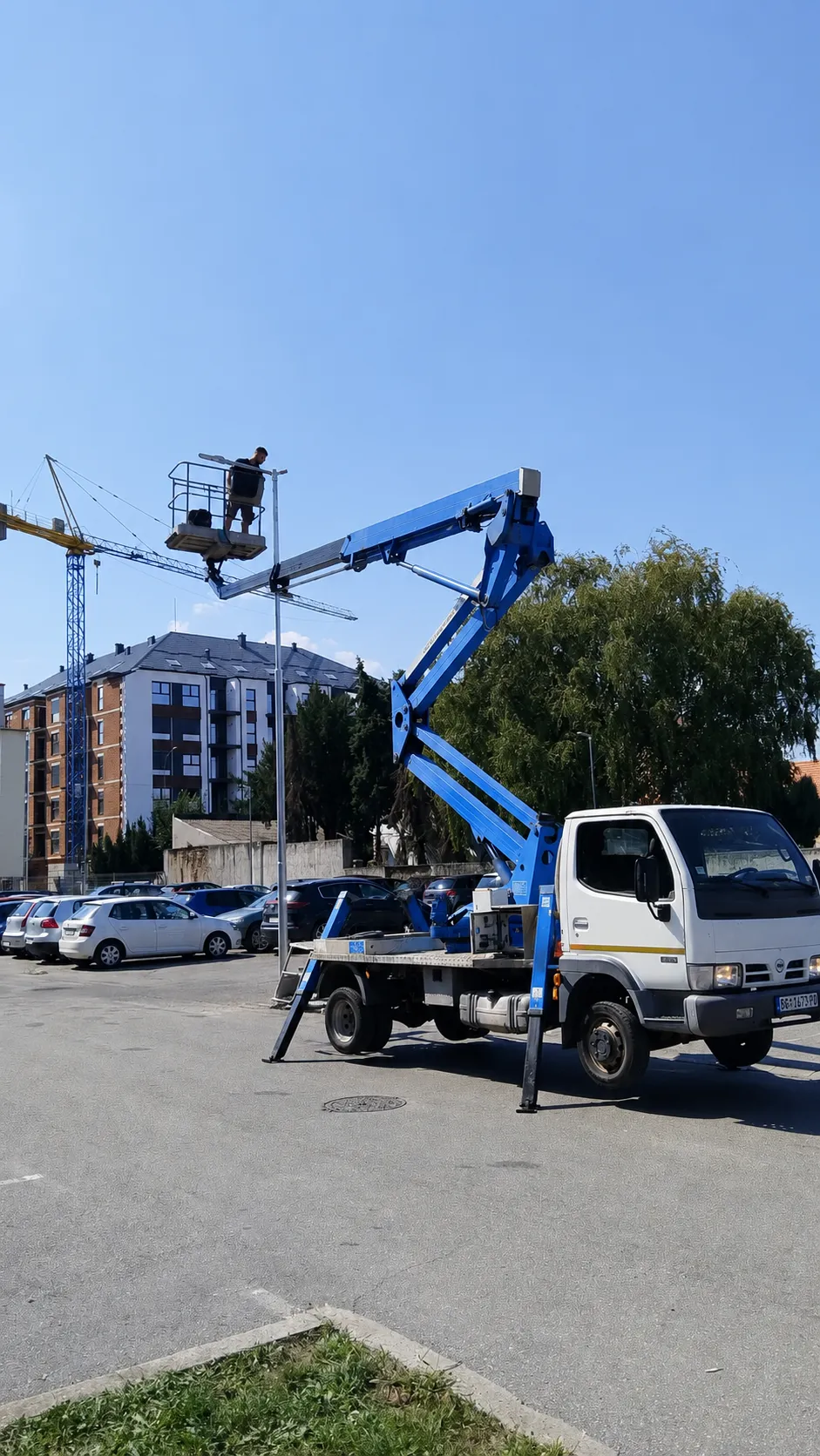 Strela izbačena do pune visine, radnik u korpi iznad parkinga